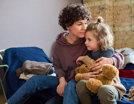 An image of a mother and daughter sat on a camp bed