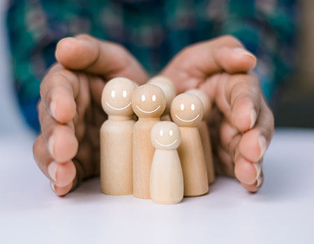 An image of hands around a family of wooden people