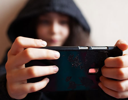 An image of a girl on a mobile device with her hood up.