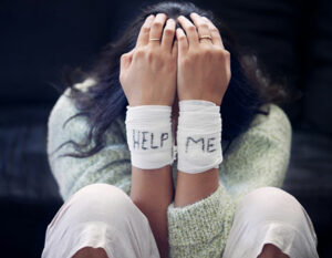 An image a girl sat on the floor with wrists bandaged with the words Help Me on them