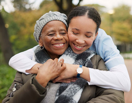 An image of a young girl hugging and older lady with smiles on their faces