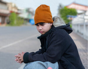 A boy say on the street in a hat looking sad