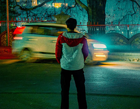 An image of a child on a dark street with a fast moving car in the background